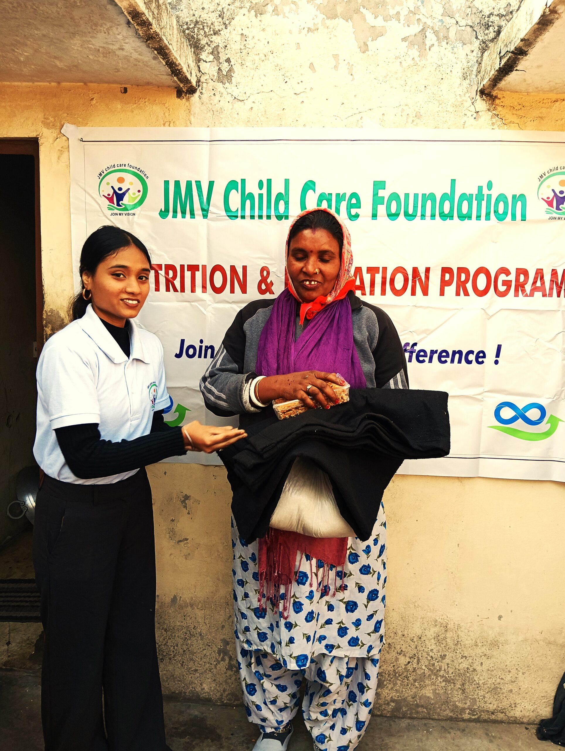 Supporter giving clothes and sweet box to a visually impaired woman , both appearing happy.”