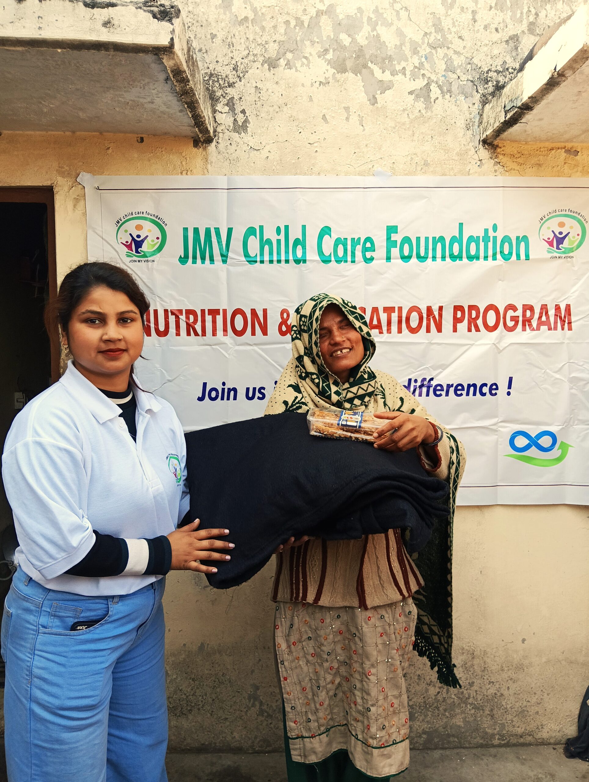 Supporter giving clothes and sweet box to a visually impaired old woman, both appearing happy.”