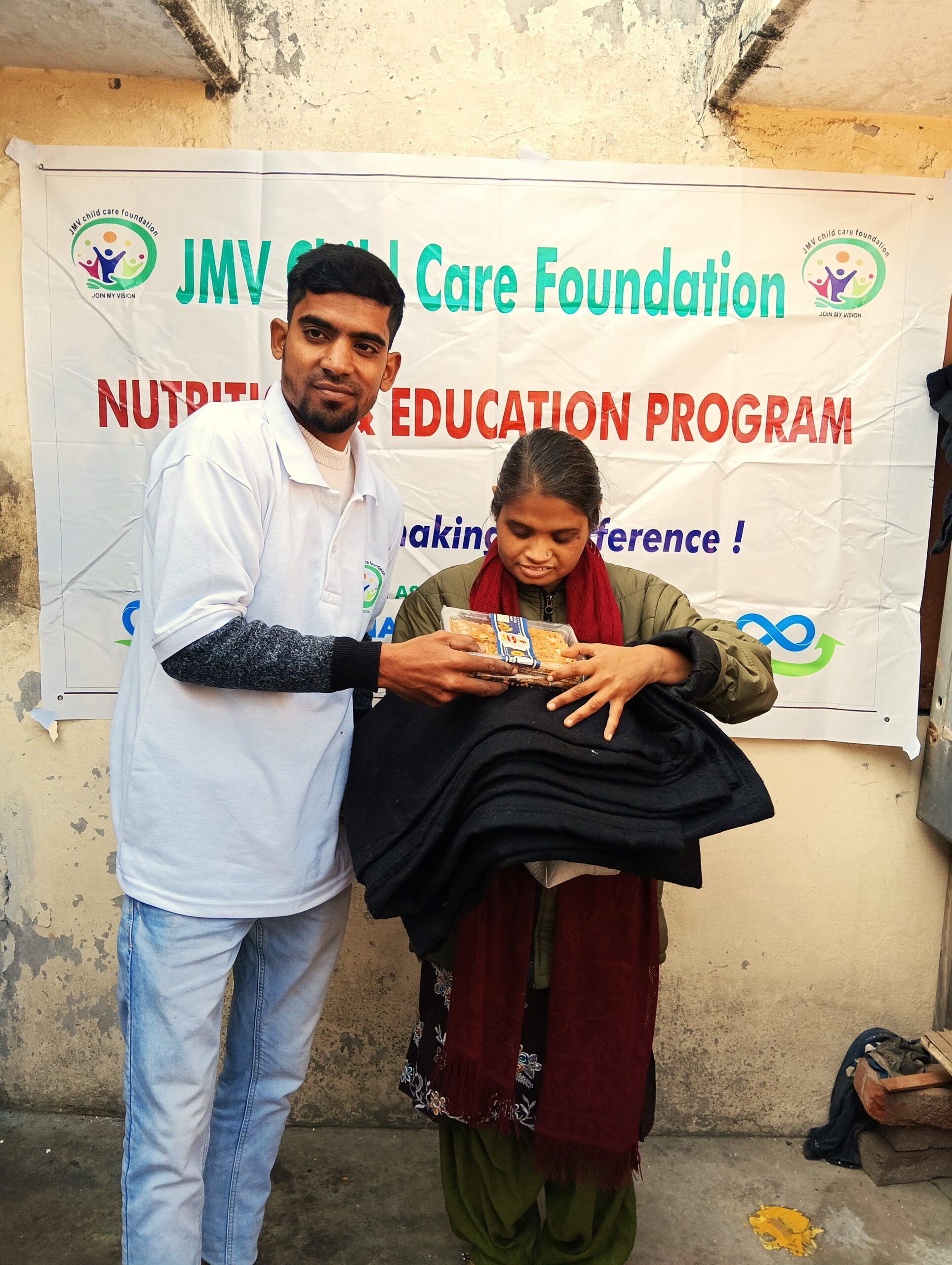 Supporter handing a clothes and sweet box to a visually impaired girl both appearing happy.”