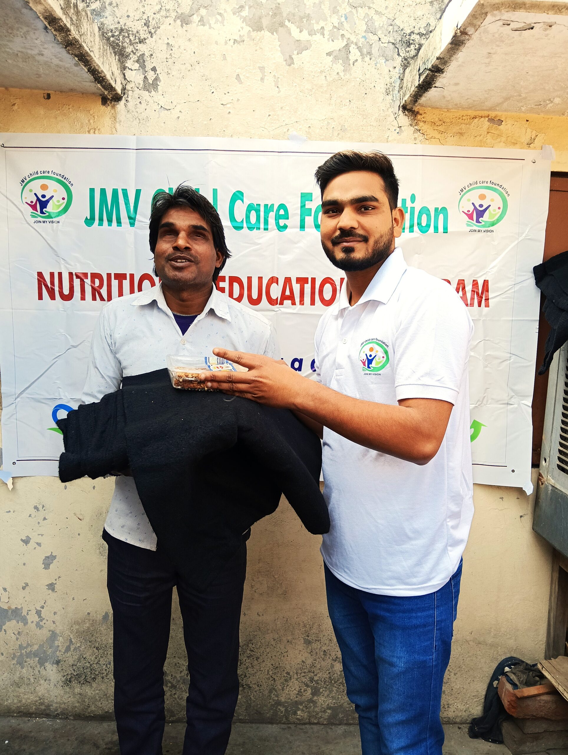 Supporter giving clothes and sweets to a visually impaired man, both appearing happy.”